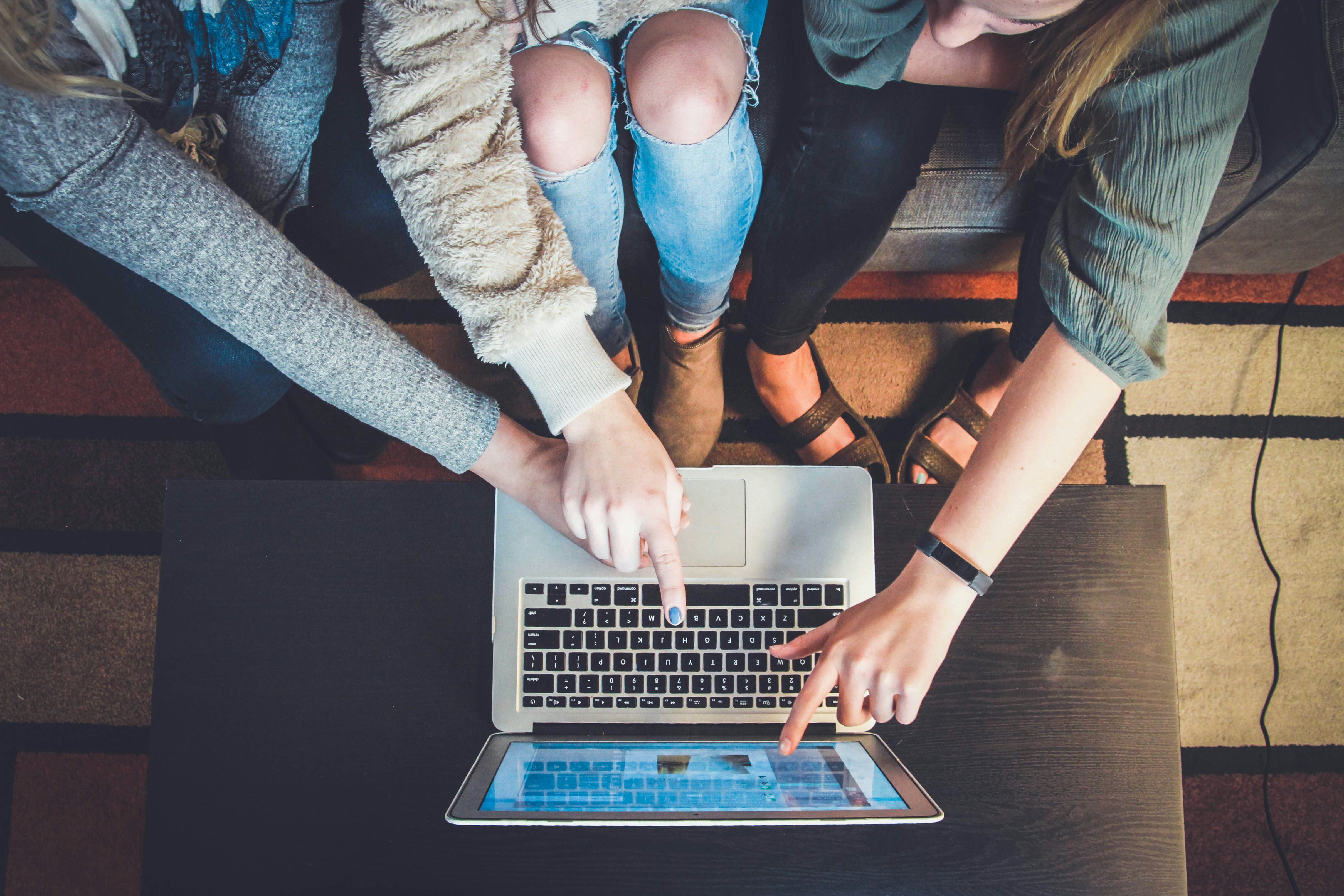 Many hands pointing towards the screen of an opened laptop