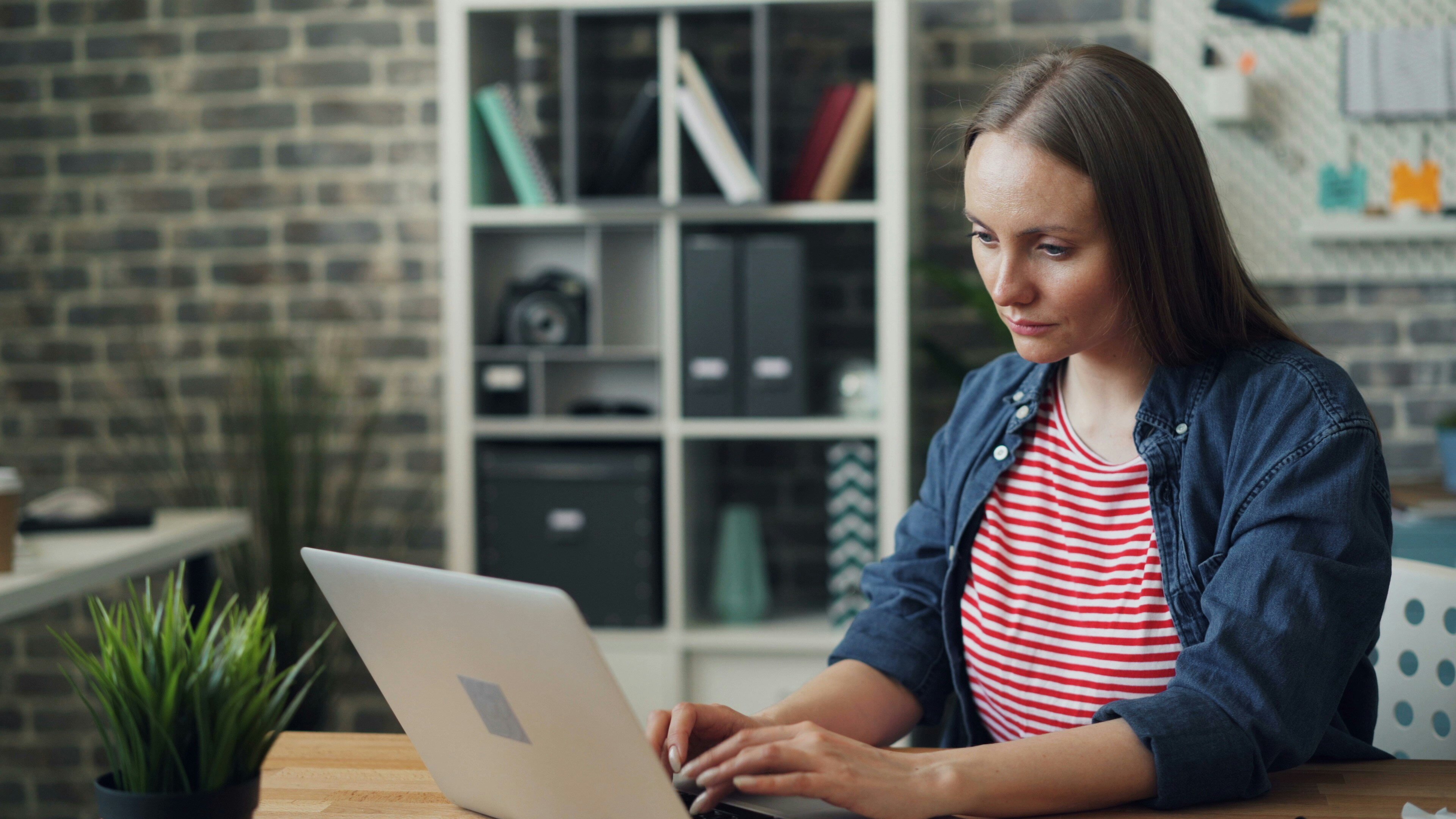 A woman looks despondently at a laptop 